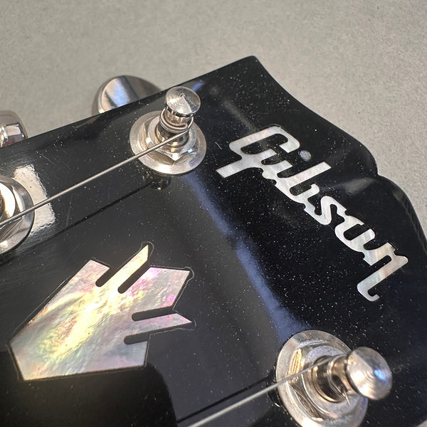 Close-up of black Gibson guitar headstock with mother-of-pearl inlay and tuning pegs