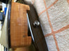 Close-up of guitar strap button and wooden neck heel on acoustic guitar body resting on a textured fabric surface with orange and cream checkered pattern.
