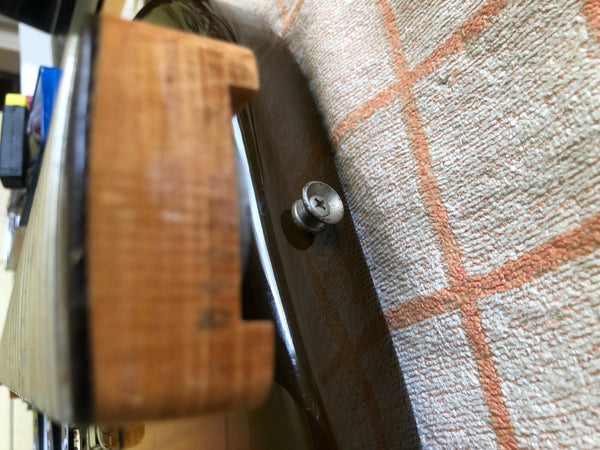 Close-up of guitar strap button and wooden neck heel on acoustic guitar body resting on a textured fabric surface with orange and cream checkered pattern.