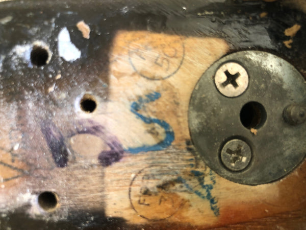 Close-up detail of vintage guitar neck plate area showing serial number markings, screws, and wood grain with visible wear and paint chipping.
