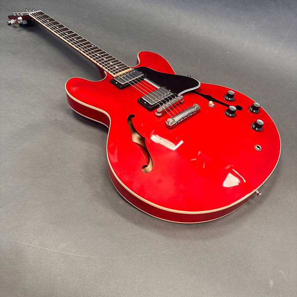 Red semi-hollow body electric guitar with double cutaway, black pickguard, dual humbucker pickups, and four control knobs on a gray surface