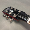 Close-up of Gibson guitar black headstock with chrome tuning pegs and pearl inlay logo on gray background