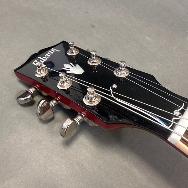 Close-up of Gibson guitar black headstock with chrome tuning pegs and pearl inlay logo on gray background