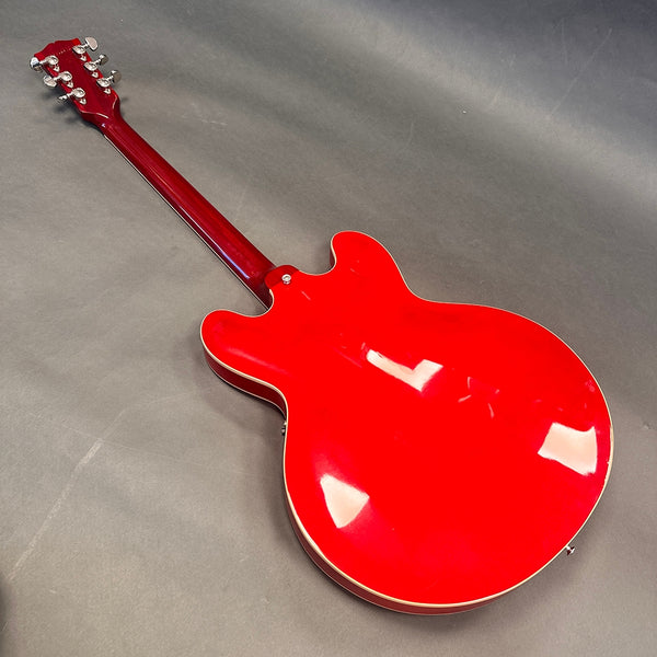 Glossy red semi-hollow electric guitar back with cream binding and six chrome tuning pegs on headstock against grey background
