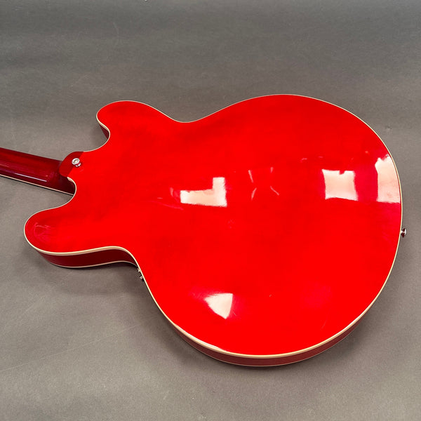 Back of bright red semi-hollow electric guitar with cream binding on gray background