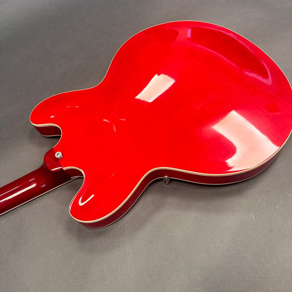 Back view of red semi-hollow electric guitar with white binding and glossy finish on gray background