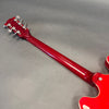 Back of red electric guitar neck with chrome tuning pegs and glossy finish on gray background