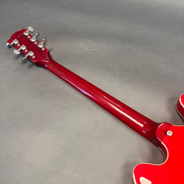 Back of red electric guitar neck with chrome tuning pegs and glossy finish on gray background