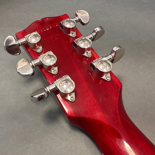 Close-up of red guitar headstock with six chrome tuning pegs and serial number, made in USA, on gray background