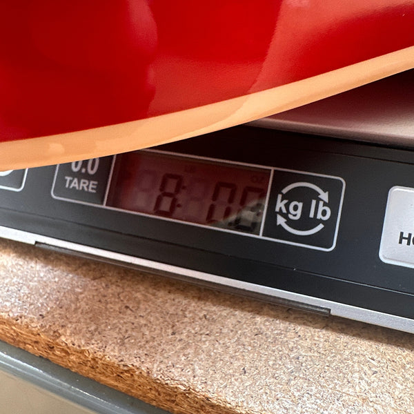 Close-up of a red guitar body being weighed on a digital scale showing 8 pounds at Coffee House Guitars.