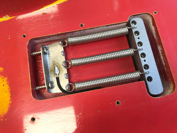 Close-up of red electric guitar tremolo spring cavity showing three metal springs and vintage-style claw plate with grounding wire