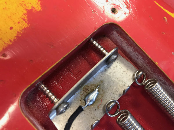 Close-up of red electric guitar tremolo cavity with springs, screws, and metal tremolo claw showing worn paint and vintage hardware details