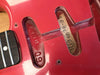 Close-up of red electric guitar body without pickups, showing neck pocket with serial number 111948899 and 60 relic stamp inside pickup cavity near rosewood fingerboard and metal frets