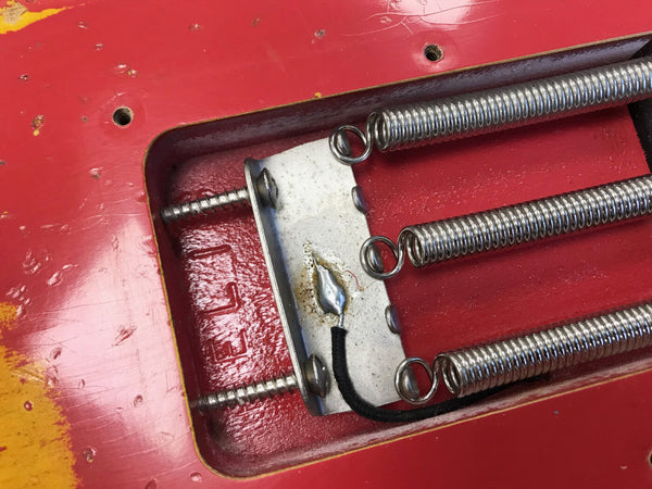 Close-up of electric guitar tremolo cavity showing three metal springs attached to claw plate inside a red guitar body