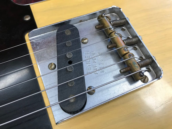 Close-up of Fender Telecaster vintage single-coil bridge pickup and metal bridge plate with adjustable brass saddles on natural wood guitar body.