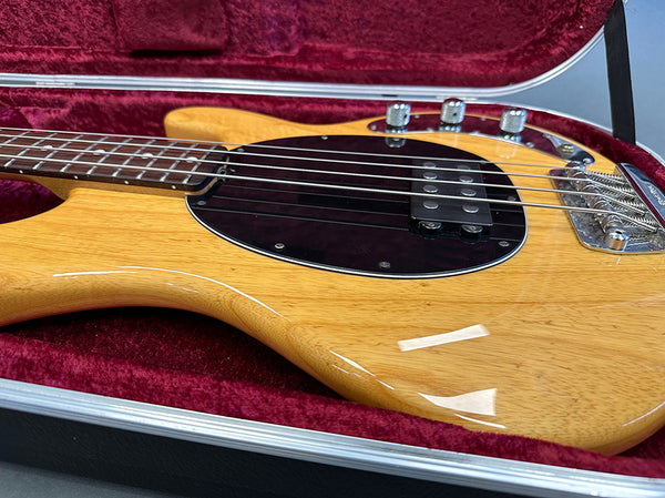 Natural wood finish electric bass guitar with black pickguard and chrome knobs in red velvet-lined hard case