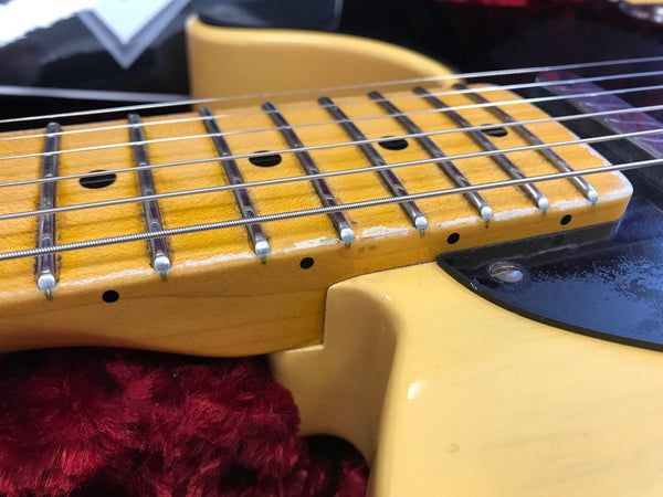Close-up of vintage yellow maple guitar neck and fretboard with steel strings and black dot inlays, laid on red plush guitar case lining.