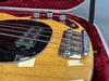 Close-up of natural wood finish electric bass guitar bridge, pickups, and control knobs in red velvet-lined guitar case