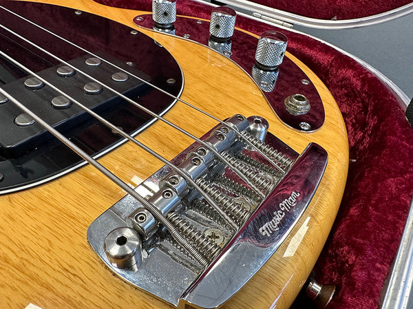 Close-up of Music Man bass guitar bridge and pickups on natural wood finish body in red velvet-lined guitar case