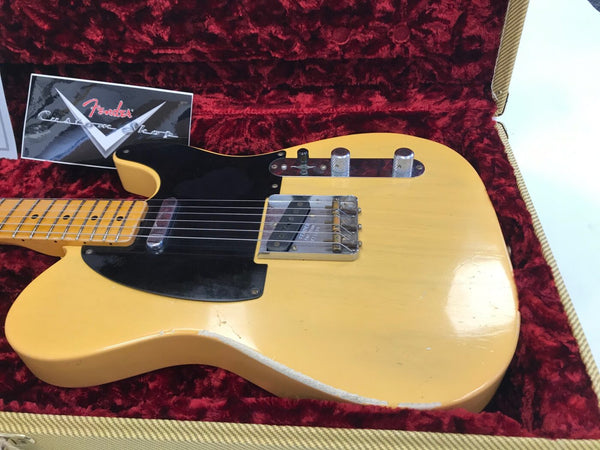 Vintage Fender Telecaster electric guitar in butterscotch blonde finish with black pickguard, displayed in a red velvet-lined tweed hard case, showing signs of wear and relic finish.
