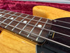 Close-up of natural wood electric bass guitar fretboard with metal strings and dot inlays in red velvet-lined guitar case