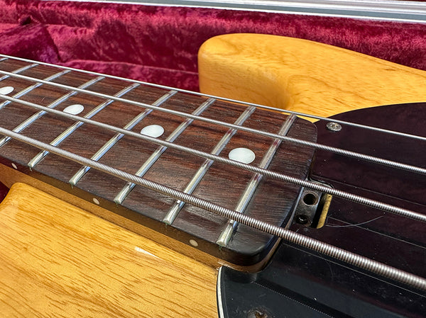 Close-up of natural wood electric bass guitar fretboard with metal strings and dot inlays in red velvet-lined guitar case