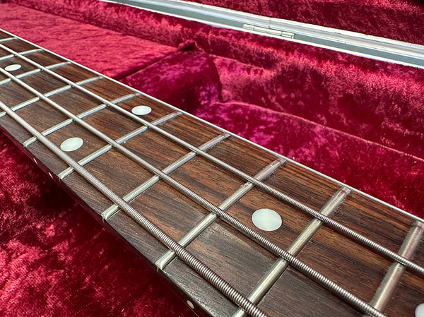 Close-up of bass guitar rosewood fingerboard with metal frets and white dot inlays in red velvet-lined case