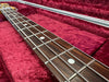 Close-up of bass guitar neck and metal frets on rosewood fingerboard with white dot inlays inside red velvet guitar case