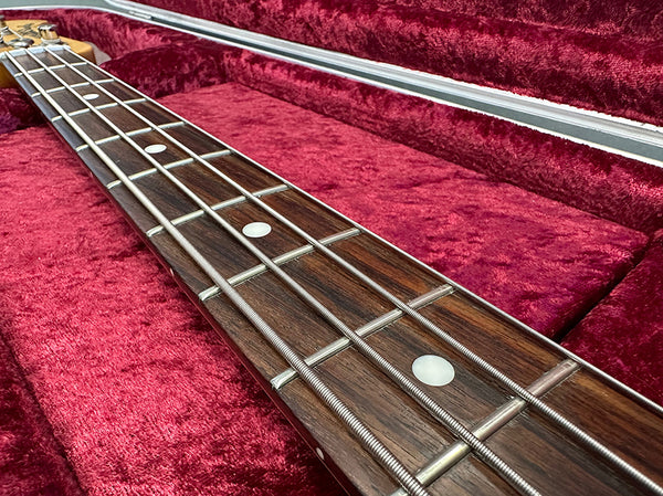 Close-up of bass guitar neck and metal frets on rosewood fingerboard with white dot inlays inside red velvet guitar case