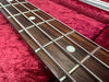 Close-up of bass guitar fretboard with metal frets and round inlay markers on rosewood, resting on red plush guitar case lining