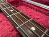 Close-up of bass guitar fretboard with metal frets and round white inlay markers against a red velvet guitar case interior