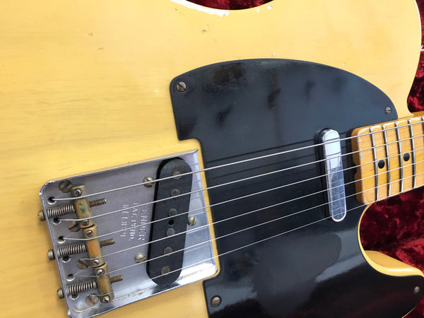Close-up of vintage Fender Telecaster electric guitar bridge, single-coil pickups, and maple fretboard with black pickguard on butterscotch blonde body