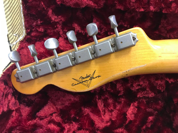 Vintage Fender Custom Shop guitar headstock with six vintage tuning pegs on a maple neck, displayed on red plush guitar case interior