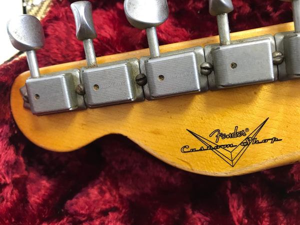 Close-up of vintage Fender Custom Shop guitar headstock with six tuning pegs and visible Fender Custom Shop logo on maple wood against red plush background