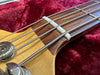 Close-up of bass guitar neck showing metal tuning pegs, steel strings, and wooden fretboard on red velvet background