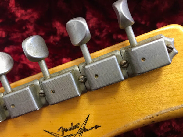 Close-up of vintage Fender guitar tuning machines on a maple headstock with red plush background