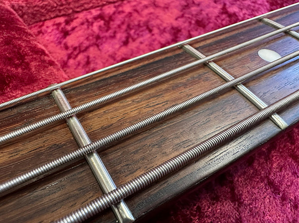 Close-up of bass guitar fretboard with metal frets and wound strings on red fabric background