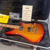 Ernie Ball Music Man electric guitar in sparkly red-orange finish with dual humbucker pickups inside a black plush-lined hard case with certificate of authenticity and accessories.