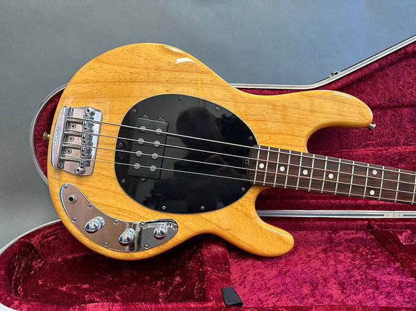 Natural finish electric bass guitar with black pickguard and chrome control knobs in red velvet-lined hard case