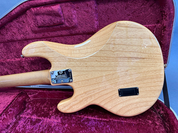 Natural wood finish electric guitar back with visible wood grain and metal neck plate, displayed inside plush red guitar case