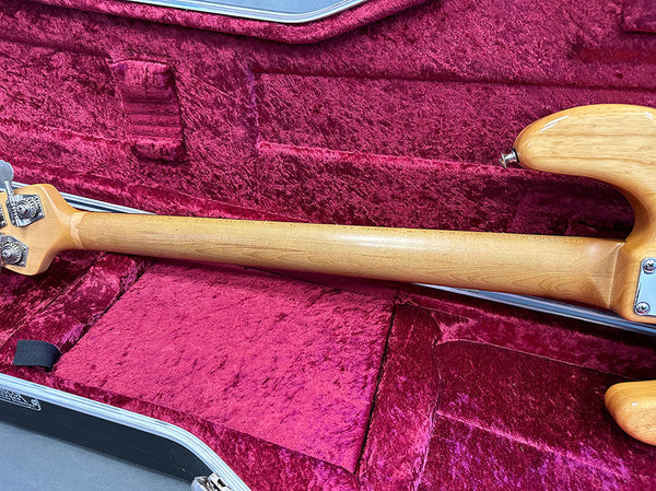 Back of light wood electric guitar neck with silver tuning pegs resting in a plush red velvet guitar case interior