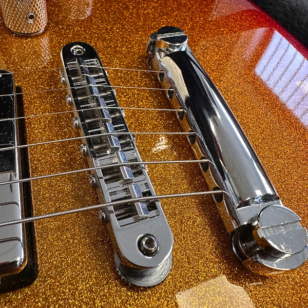 Close-up of chrome bridge and tailpiece on electric guitar with gold sparkle finish and metal strings