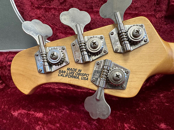 Close-up of guitar tuning pegs on wooden headstock with "Made in San Luis Obispo California, USA" stamp, resting on red velvet background