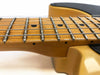 Close-up of maple guitar neck and fingerboard with metal frets and steel strings on a cream-colored electric guitar body