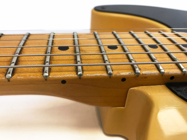 Close-up of maple guitar neck and fingerboard with metal frets and steel strings on a cream-colored electric guitar body