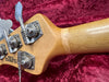 Close-up of natural wood bass guitar headstock with four vintage-style tuning pegs on red velvet background, made in San Luis Obispo California USA.
