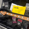 Ernie Ball Music Man guitar neck with pearl block inlays inside black plush guitar case, including Ernie Ball and Strings & Things inspection tags, and yellow Music Man battery replacement instruction sheet.