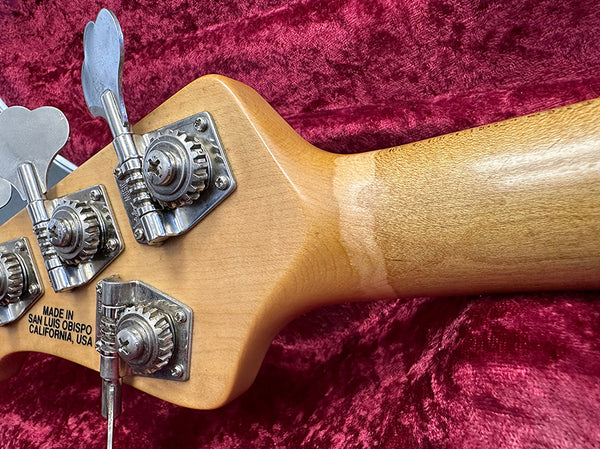 Close-up of natural wood bass guitar headstock with four vintage-style tuning pegs on red velvet background, made in San Luis Obispo California USA.