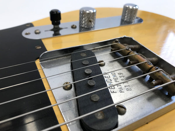 Close-up of Fender Telecaster bridge and pickup with metal plate and guitar strings on butterscotch finish body