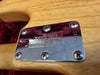 Close-up of Ernie Ball Music Man neck plate with serial number E16631 on natural wood electric guitar body